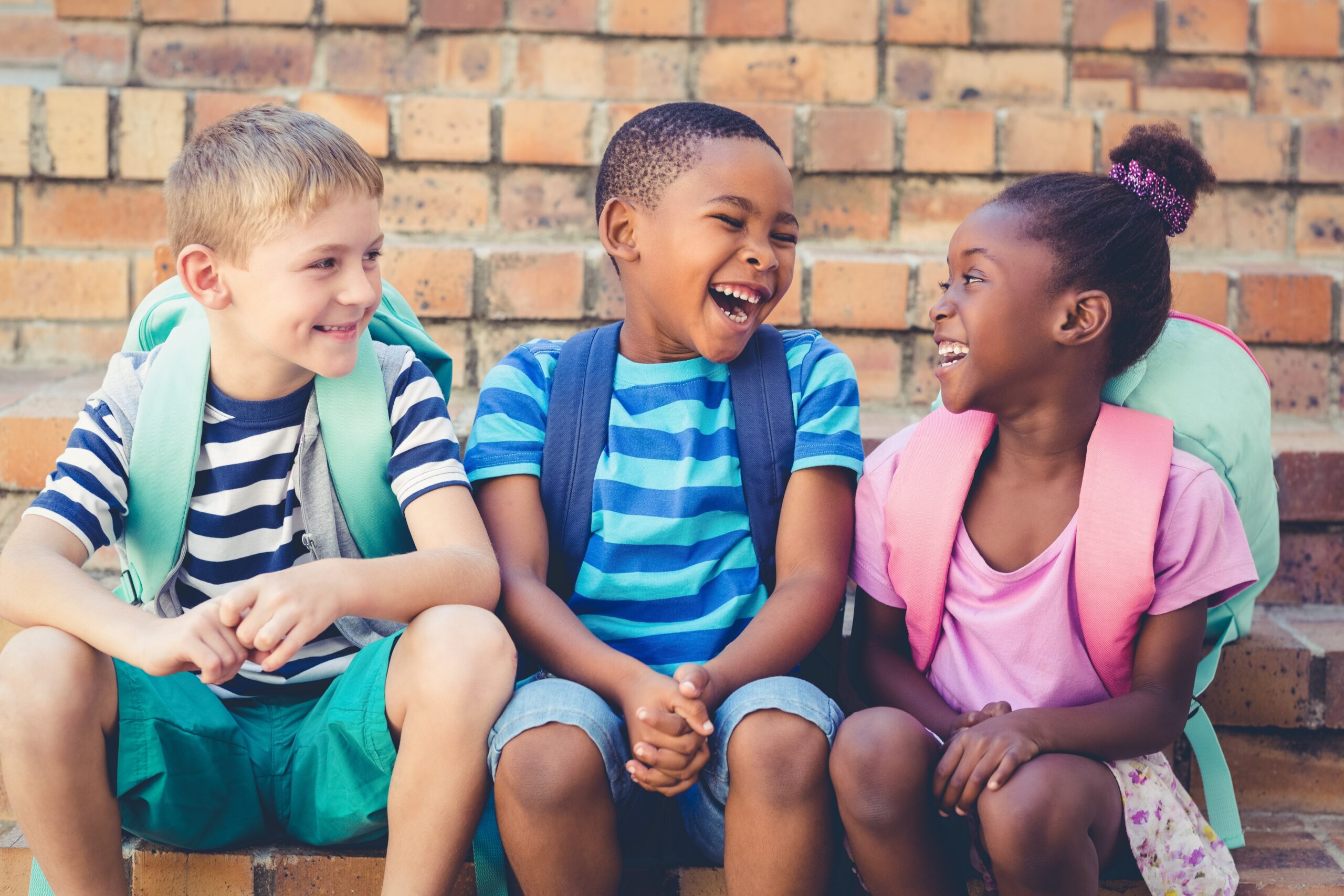 Happy mixed race school kids sitting together on staircase kids with backpacks
